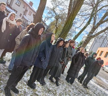 Dwór. Grupa osób stoi na dworze, między drzewami