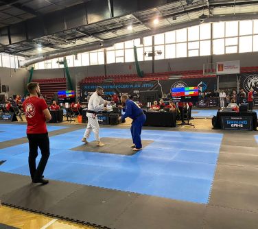 Hala sportowa. Na piankowej macie walczy dwóch mężczyzn, obok nich sędzia.