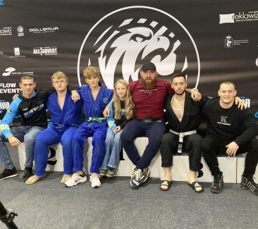 Siedem osób siedzi na podium, trzymają się za ramiona