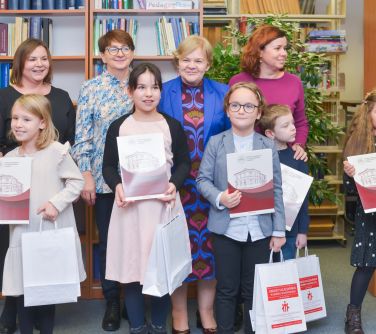 Czytelnia. Cztery kobiety, przed nimi pięcioro dzieci. Dzieci trzymają w dłoniach teczki i torby papierowe