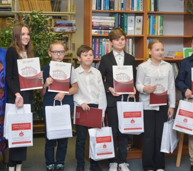 Czytelnia. Kobieta i sześcioro dzieci pozuje do zdjęcia. Dzieci trzymają w dłoniach teczki oraz torby papierowe