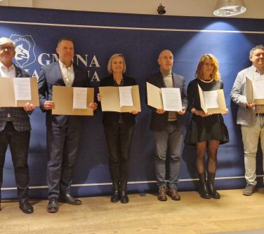 Pomieszczenie. Sześć osób trzyma przed sobą otwarte teczki z dokumentami
