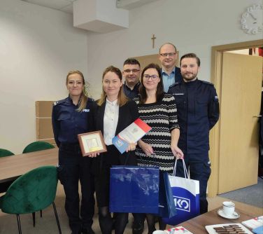 Sala w bibliotece. Sześć osób pozuje do zdjęcia. Dwie kobiety w środku trzymają upominki i dyplom