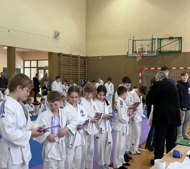 Hala sportowa. Grupa dzieci w kimonach otrzymuje czekolady
