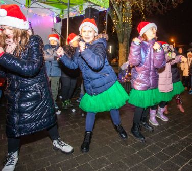 Na dworze wieczór. Grupa dziewczynek w czapkach mikołajkowych przedstawia układ taneczny