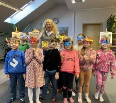 Pomieszczenie. Kobieta i jedenaścioro dzieci w maskach karnawałowych pozują do zdjęcia