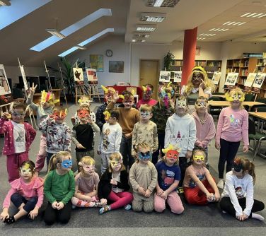 Pomieszczenie, czytelnia. Kobieta oraz 22 dzieci pozuje do zdjęcia w maskach karnawałowych