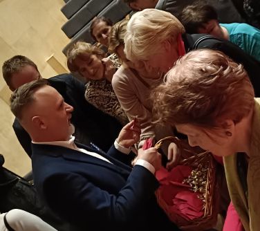 Sala koncertowa. Mężczyzna z koszykiem rozdaje upominki wychodzącym widzom