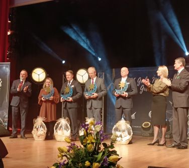 Na scenie stoi siedem osób. Cztery osoby w środku trzymają w dłoniach nagrody w kształcie księżyca, przed nimi kosze...
