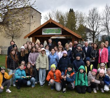 Na trawniku. Grupa dorosłych i dzieci pozuje do zdjęcia. W tle drewniana wiata z napisem "Wiata przyrodnicza".