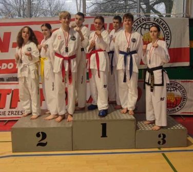 Hala sportowa. Na podium w kimonach pozuje ośmiu zawodników