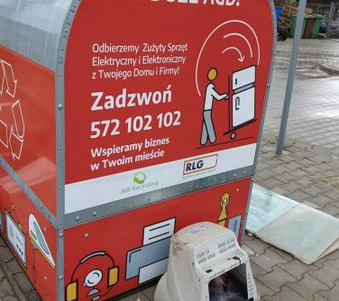 Na dworze. Czerwony pojemnik na elektroodpady stoi na chodniku