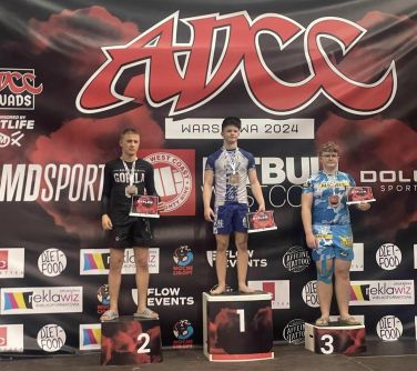 Hala sportowa. Na podium trzech młodych zawodników z medalami na szyi i dyplomami w dłoniach