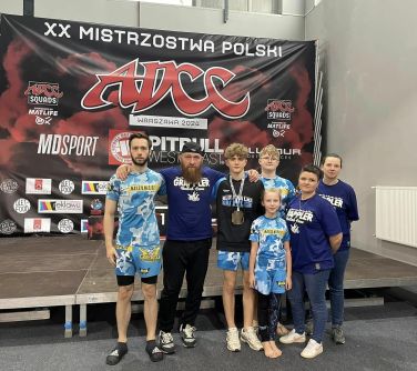 Hala sportowa. Przed mini sceną grupa siedmu osób pozuje do zdjęcia