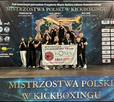 Grupa osób w sportowej pozie pozuje do zdjecia. Z przodu dwie osoby trzymają baner.