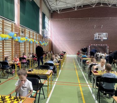 Sala gimnastyczna. Stoły ustawione jeden za drugim. na stołach aszchy. Dzieci rozgrywają partie. Po lewej na drabinkach...