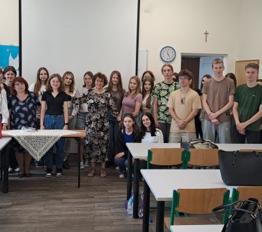 Sala lekcyjna. Grupa osób pozuje na przodzie kalsy. Na ławkach stoją torby