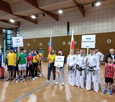 Aula sportowa. Grupy zawodników z różnych państw trzymają flagi i tabliczki z nazwami