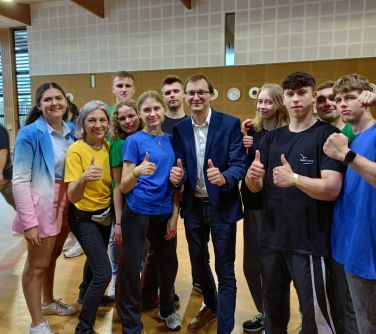 Aula sportowa. Jedenaście uśmiechniętych osób pozuje z kciukami do góry