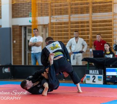 Hala sportowa. Dwóch mężczyzn z ciemnych kimonach walczy na macie