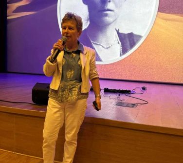 Oświetlona aula. Przed sceną przemawia kobieta