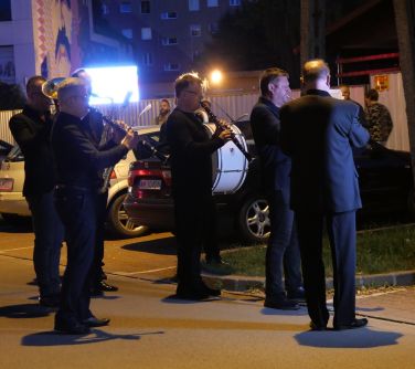 Nocą, na ulicy pięciu członków orkiestry gra na bębnie, trąbce i klarnetach