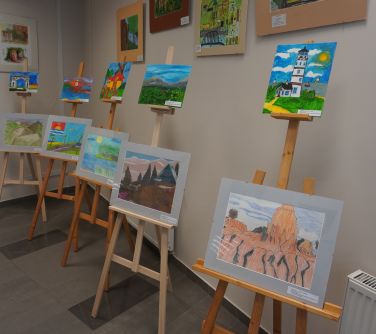 Wnętrze biblioteki. Na sztalugach znajdują się prace plastyczne z krajobrazami.