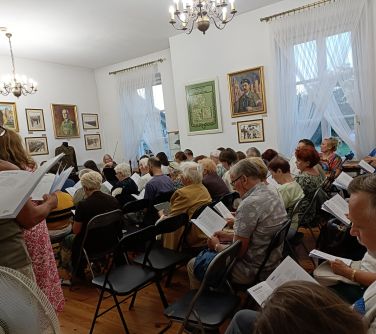 Pomieszczenie. Osoby siedzą w rzędach na krzesłach. Czytają kartki