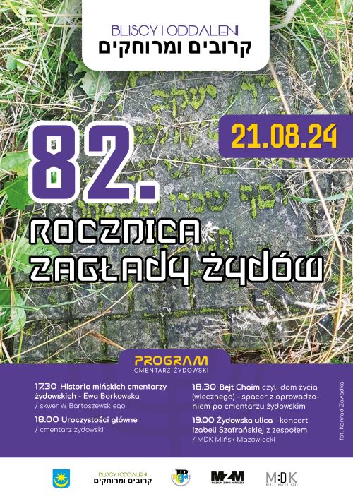 W tle tablica nagrobna pokryta trawą. Naokoło treść