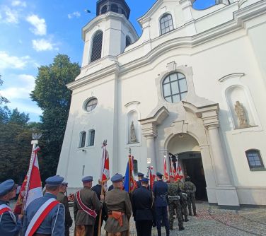 Na zewnątrz, poczty sztandarowe mundurowych stoją przed kościołem.