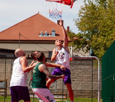 Dwór. Mężczyzna skacze do piłki po koszem do koszykówkii. Obok trzech mężczyzn przygotowanych do skoku. Patrzą na piłkę