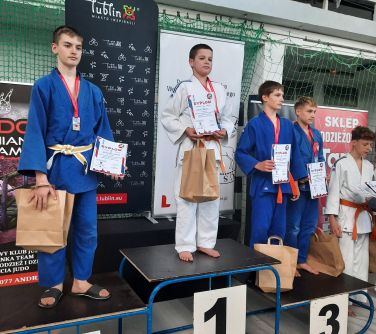 Pomieszczenie. N podium czterech chłopców w kimonach. Po lewej poza podium jeden nastolatek. W dłoniach dyplomy