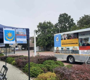 Na dworze, w ciągu dnia. Po lewej widok na niebieski namiot. Po prawej widok na oklejony ambulans