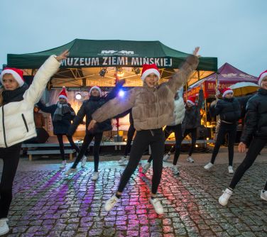 Na dworze, wczesny zmierzch. Przed scena na betonowym chodniku tańcza nastolatki w czapkach mikołaja