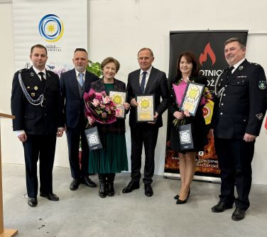 Oświetlone pomieszczenie. Grupa osób . Po środku trzy osoby dyplomy