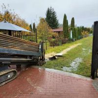 Widok na działki. Pochmurny dzień. W bramie maszyna opuszcza metalowe pręty