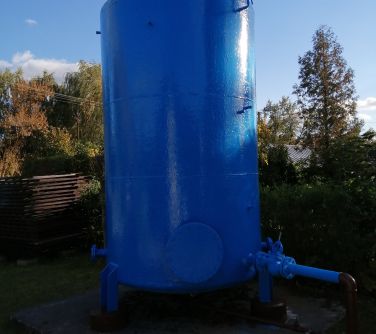 Działki, dzień, słońce. Na betonie wysoki niebieski bojler