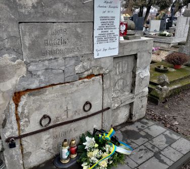 Cmentarz, dzień. Kwiaty i znicze przed kamiennym pomnikiem