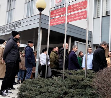 Pochmurny dzień. Pzed jasnym budynkiem urzędu miasta zgromadzone osoby