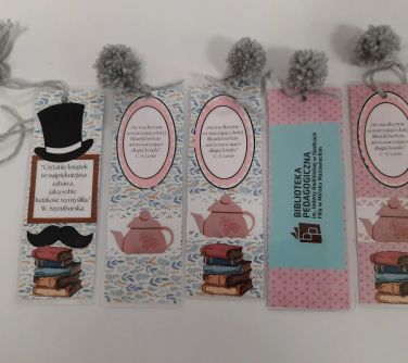 Na jasnym tle leży pięć zakładek do książki. Każda zakończona szarym pomponem z włóczki