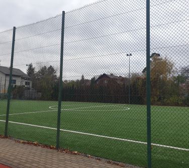 Na dworze, pochmurny dzień. Wysoka krata. Za kratą boisko