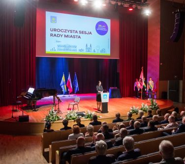 Oświetlona sala koncertowa. Widok na scenę i od tyłu widownia. Na scenie po lewej fortepian, po środku mównica i przed nią...