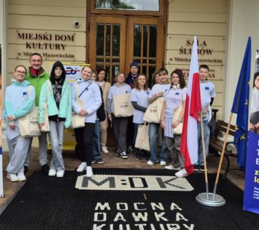 Na zewnatrz. Grupa młodzieży w białych koszulkach pozuje do zdjęcia. Stoją przed zabytkowym pałacem.