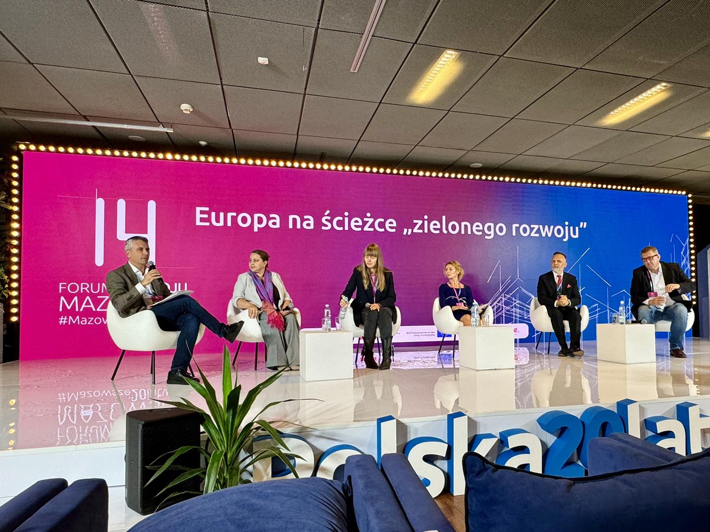 Pomieszczenie. Na scenie sześć osób siedzi na fotelach. Trwa debata. W tle różowo-niebieska duża ścianka