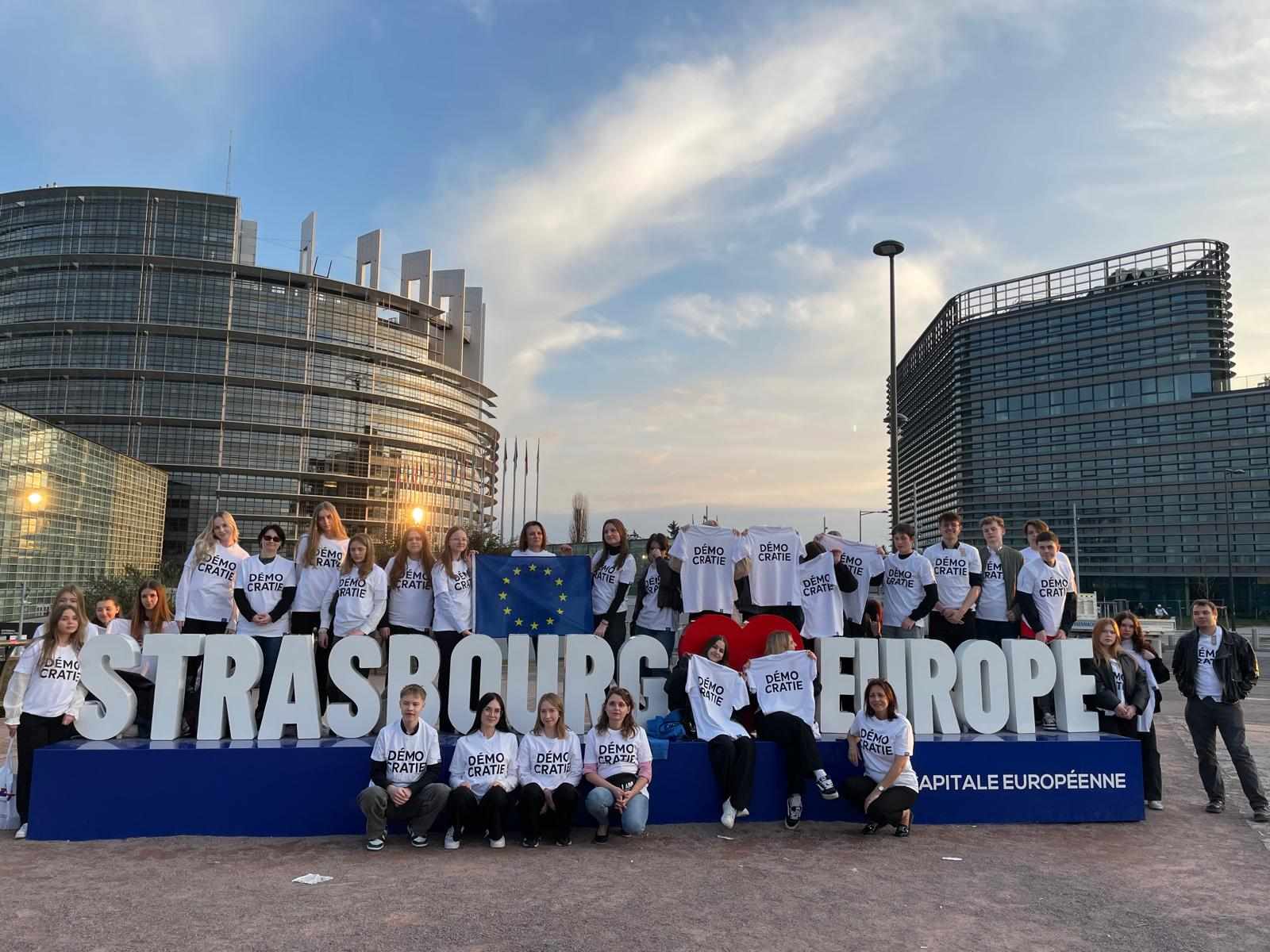 Na dworze, dzień. Grupa osób w białych koszulkach pozuje przy dużym białym napisie Strasbourg Europe